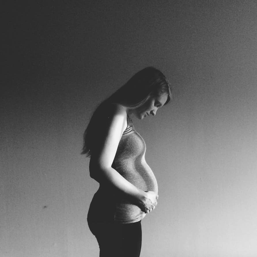 Prenatal & Postpartum Counselling 1 Young pregnant woman with postpartum depression looking lovingly down at her belly